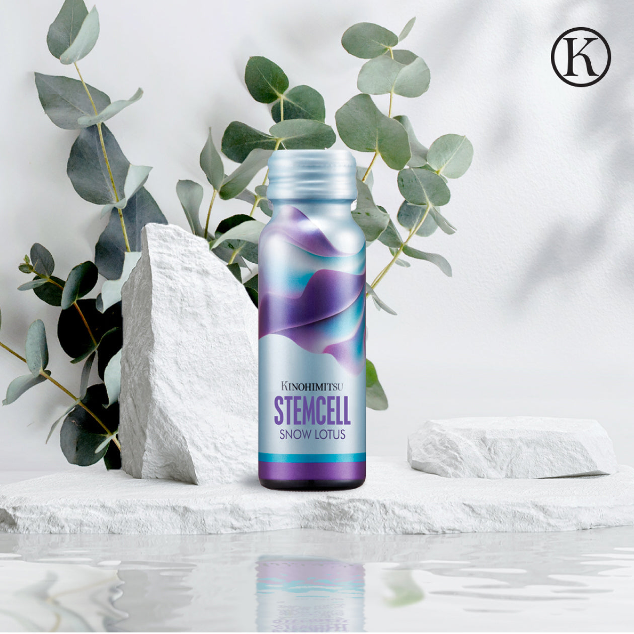 Kinohimitsu StemCell Snow Lotus bottle displayed amidst eucalyptus leaves and white textured stones, reflecting nature-inspired elegance in a minimalist setting.