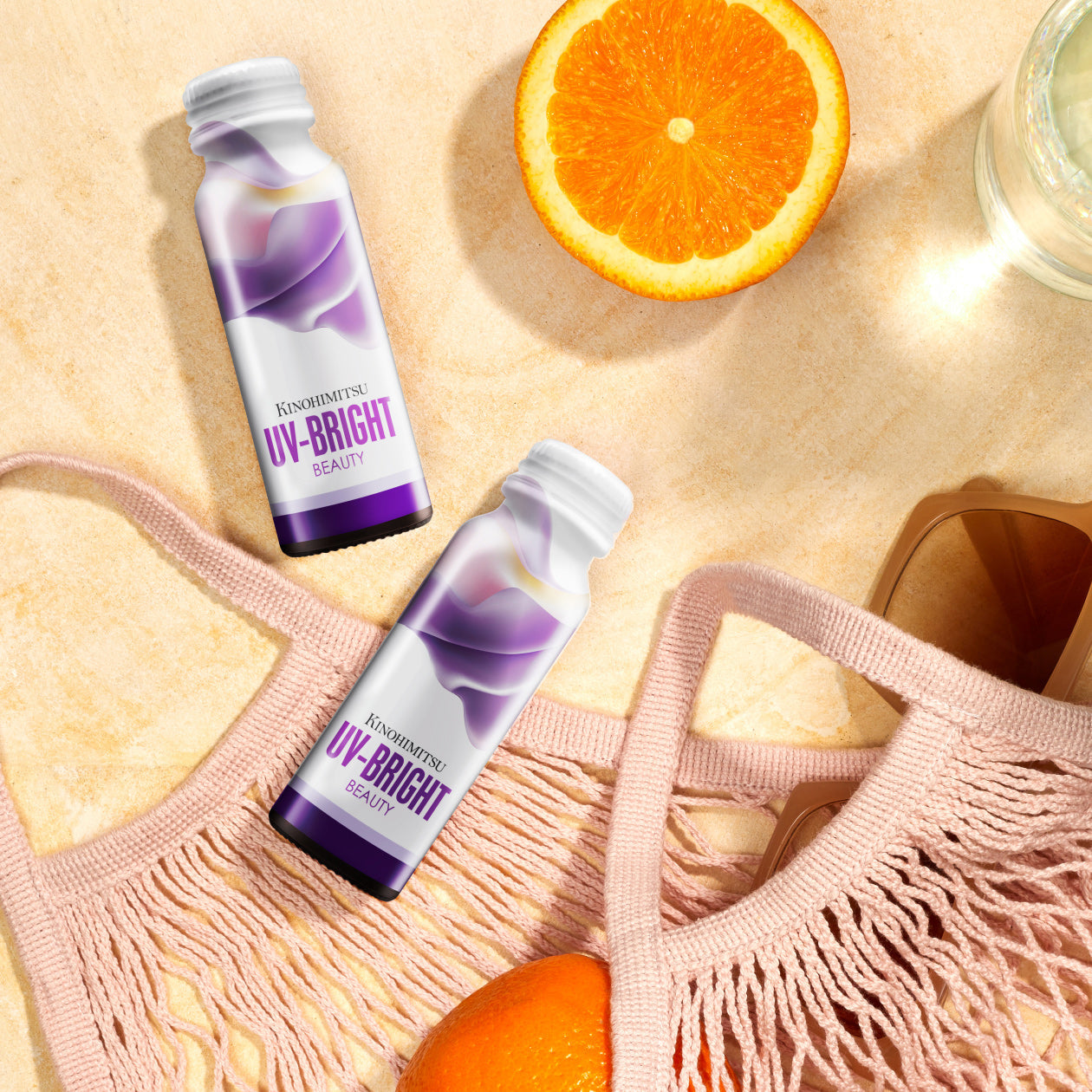 Bottles of Kinohimitsu UV Bright Beauty drink on a sunlit surface with sunglasses, an orange slice, and a pink woven bag, emphasizing summery skincare essentials.